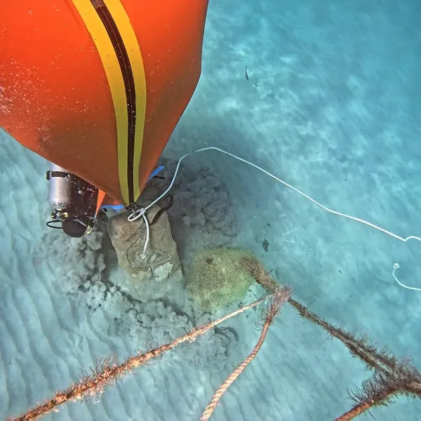 Diver rigging an orange lift bag to a concrete mooring block on a sandy seabed