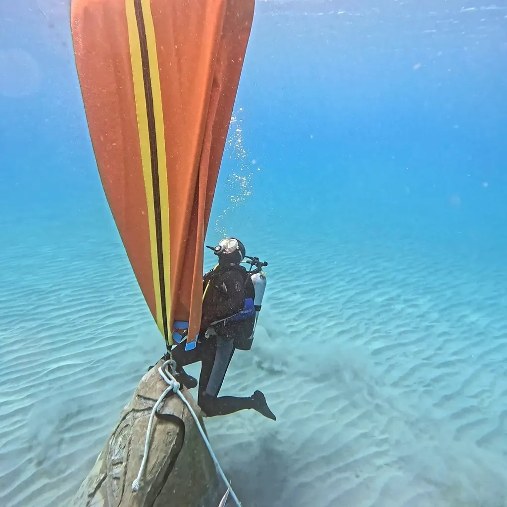 A diver working beneath an orange lift bag over a mooring block on the seabed